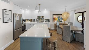 Una cocina moderna con una isla central, electrodomésticos de acero inoxidable y una zona de comedor con sillas de mimbre.