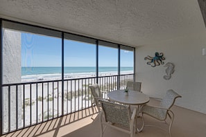 A balcony with a view of the beach, a round table, two chairs, and a wall decoration. - Sea Oats 352 | 2BR/2BA Gulf-Front Luxury Retreat (Boca Grande)