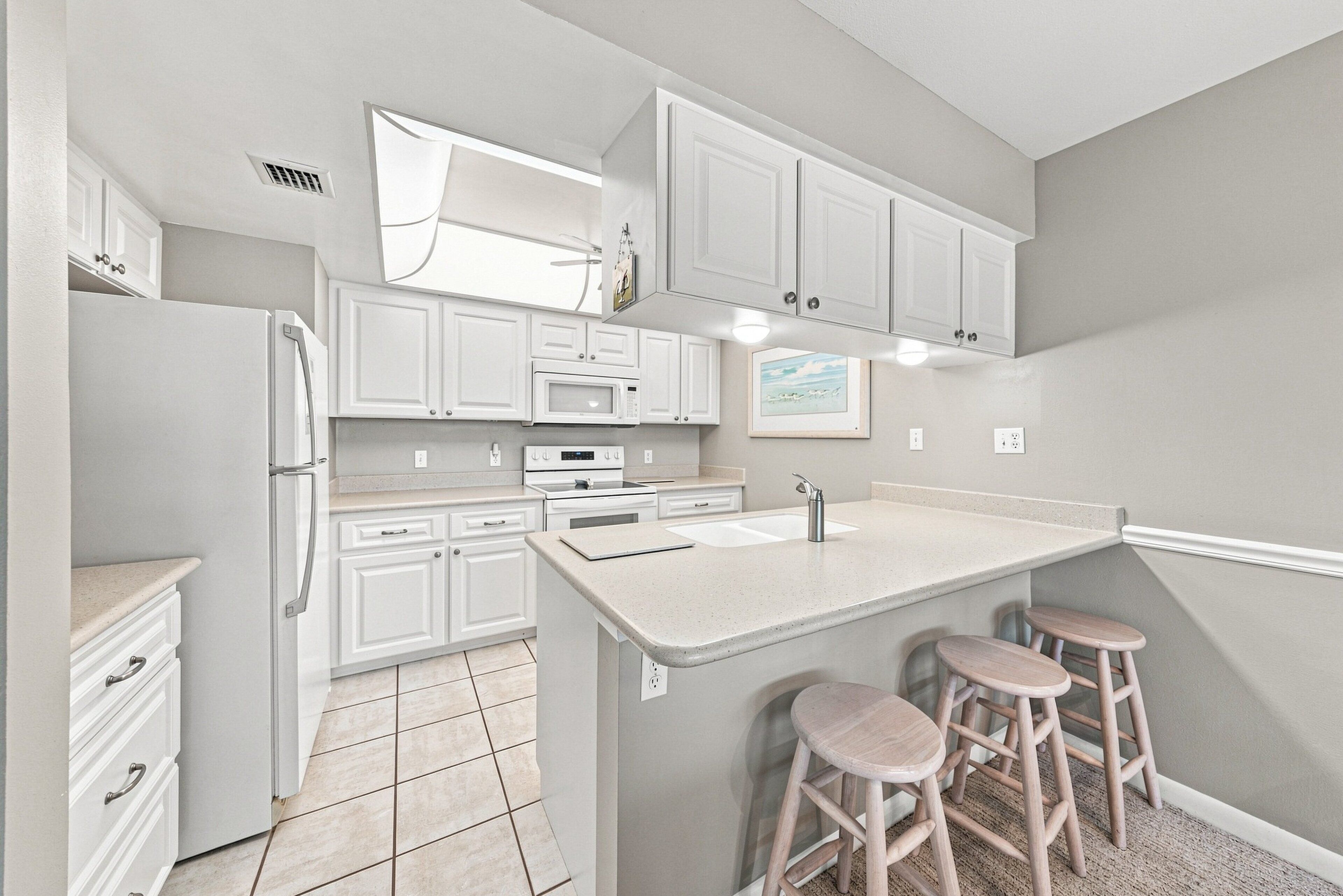 A modern kitchen with white cabinetry, a central island with stools, and a microwave.