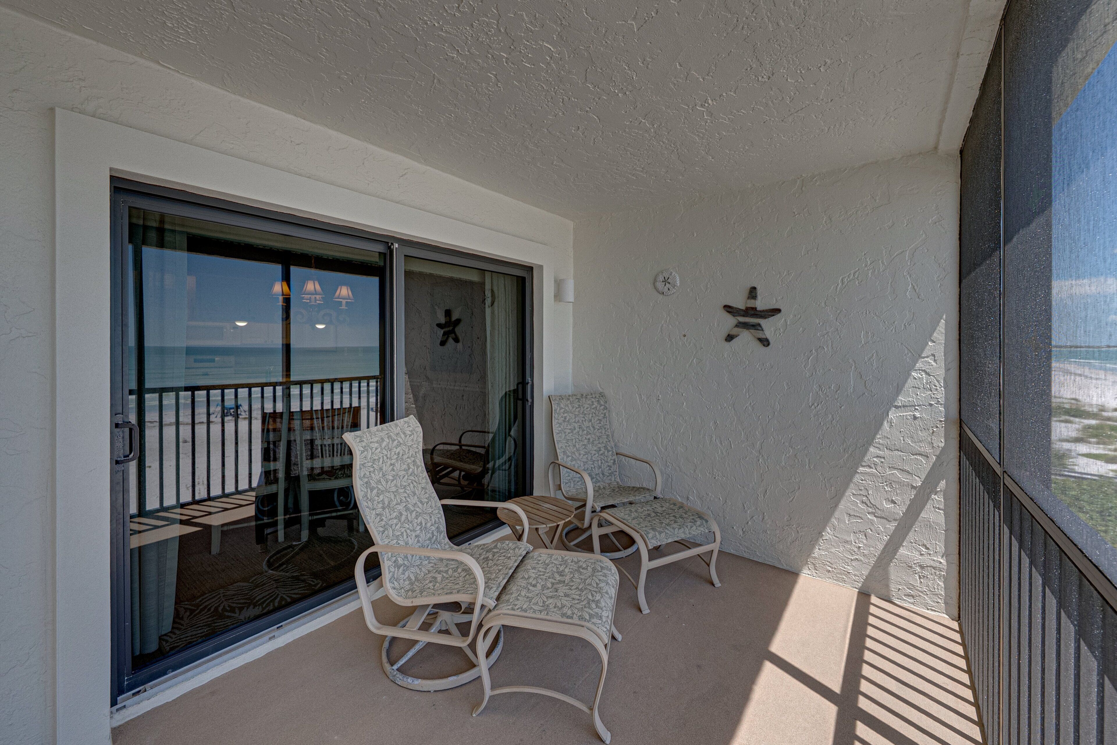 A balcony with two wicker chairs, a small table, and a sliding glass door leading to a beach view.