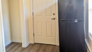 A kitchen with a black refrigerator, a white door, and wooden flooring.
