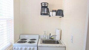 A compact kitchen with a stove, sink, and a small shelf above the sink.