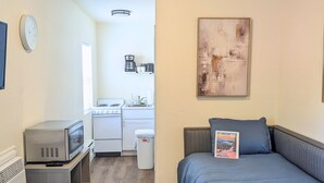 A compact room with a kitchenette, a bed with a welcome sign, a clock, and a painting on the wall.