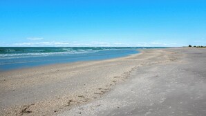 Une vaste plage de sable fin, avec des vagues douces et un ciel bleu dégagé.