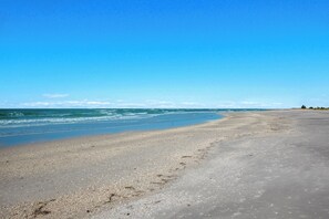 Ein weiter, sandiger Strand mit sanften Wellen und blauem Himmel.