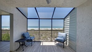 Un balcón techado con dos sillas y una mesa, con vista a la playa.