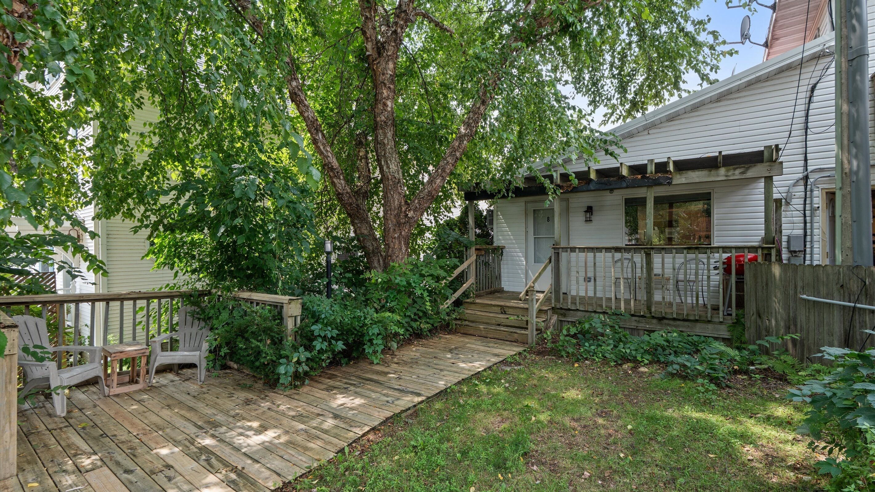 A wooden deck leading to a house with a porch and a staircase.