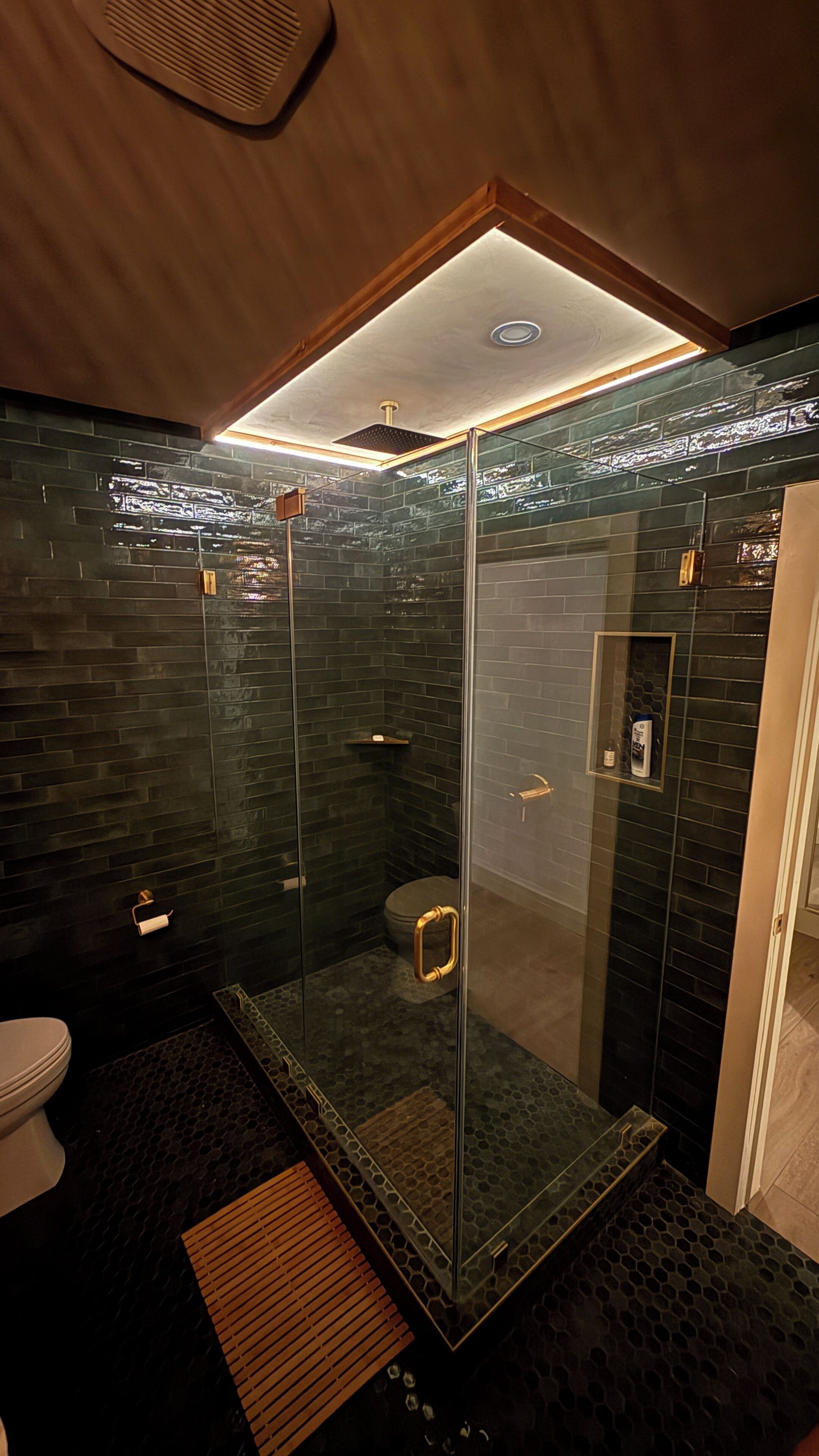Une salle de bain moderne avec une douche à parois de verre, des murs recouverts de carreaux foncés et un plancher en bois.