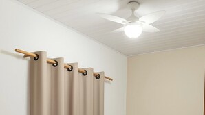 Un dormitorio con cama, cortinas color beige y ventilador de techo.