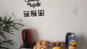 Una mesa de desayuno con pan, manzanas, plátanos, una cafetera y un cartón de leche.