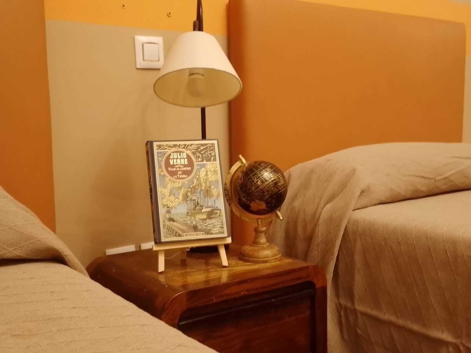 Una mesita de noche con una lámpara, un libro enmarcado y un globo terráqueo.