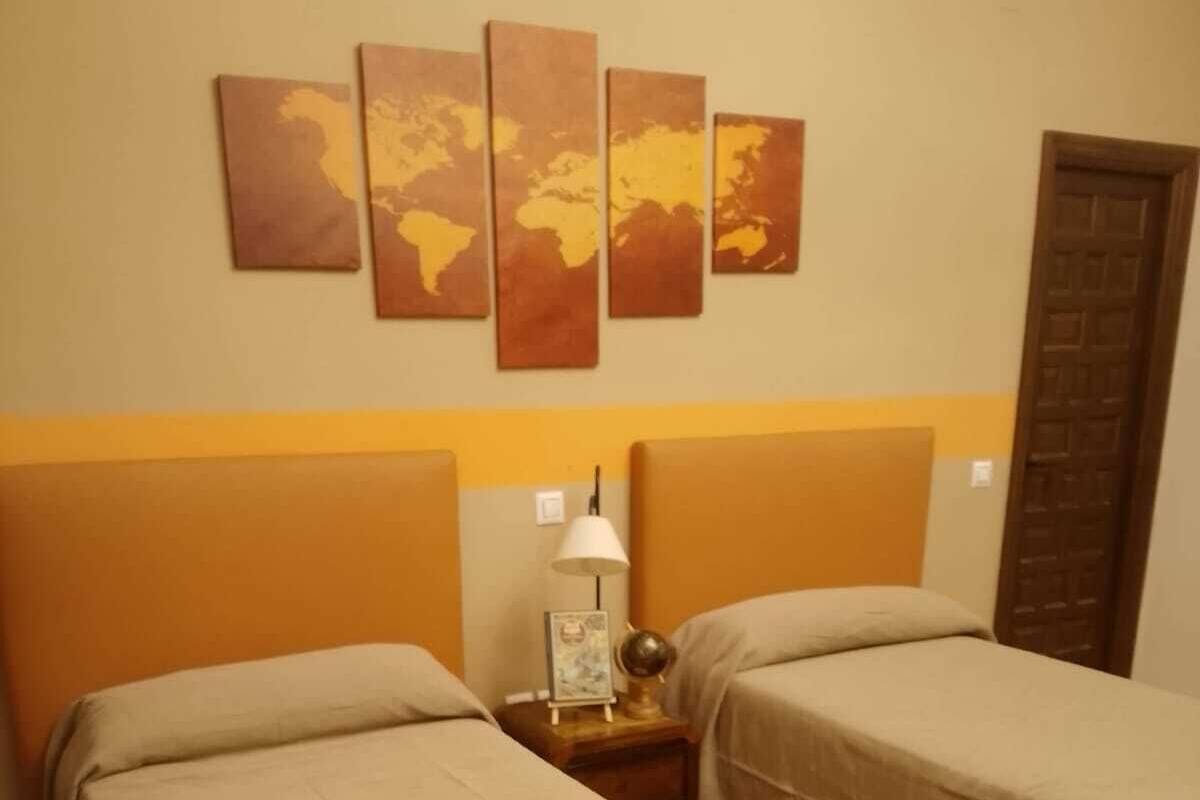 A hotel room with two beds, a nightstand with a lamp, and a world map artwork on the wall.