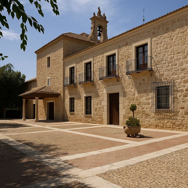A stone building with multiple balconies, a bell tower, and a courtyard with a potted plant.