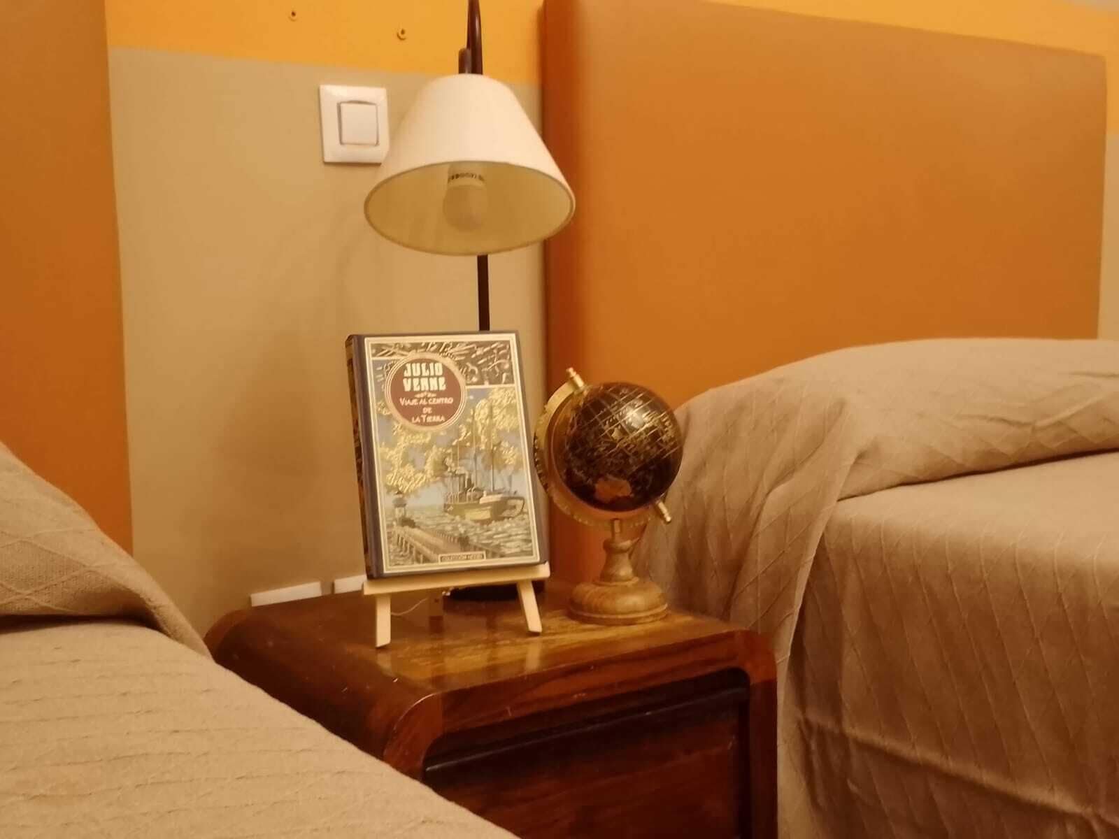 Una mesita de noche con una lámpara, un libro enmarcado y un globo terráqueo.