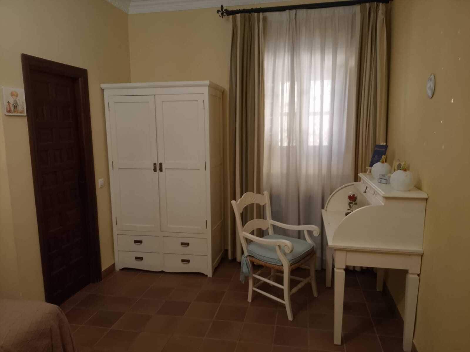 A room with a wardrobe, a chair, a table, and a bed.