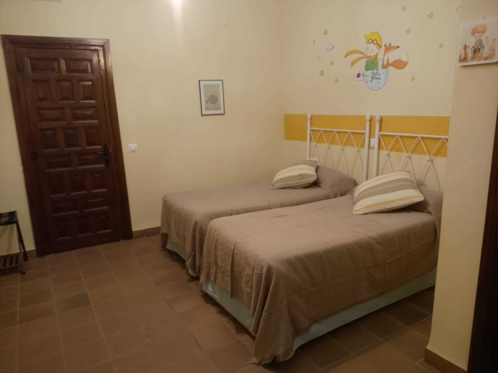 Une chambre avec deux lits simples, une porte en bois, un tableau encadré au mur et une petite fenêtre.