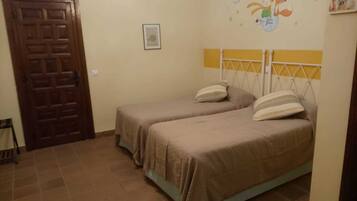 Una habitación con dos camas individuales, una puerta de madera, un cuadro enmarcado en la pared y un ventanal pequeño.