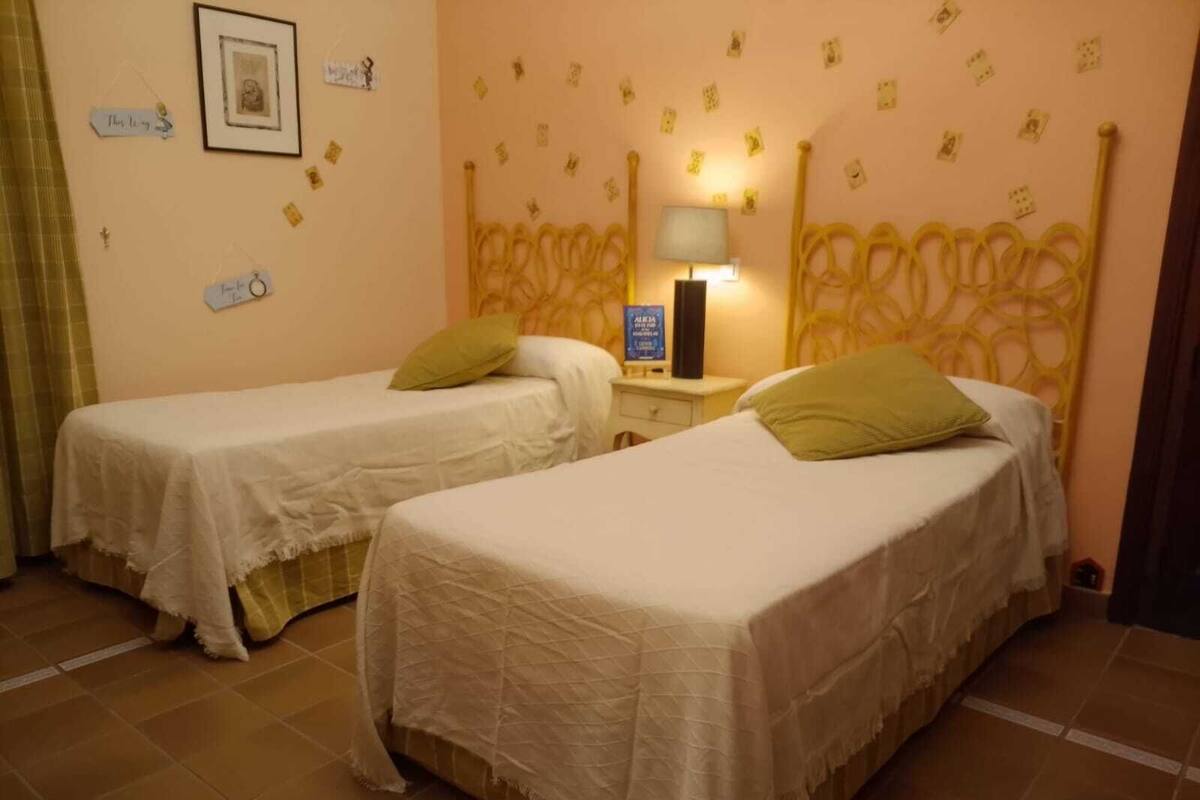 A room with two single beds, a nightstand with a lamp, and a wall with small decorative items.