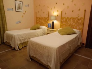 A room with two single beds, a nightstand with a lamp, and a wall with small decorative items.