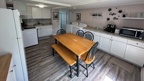 A compact kitchen with white cabinets, a wooden dining table, and a microwave on the countertop.