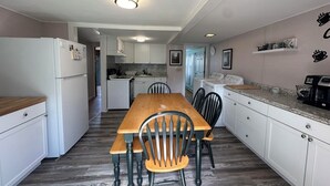 A compact kitchen with a wooden table and chairs, white cabinets, and a refrigerator.