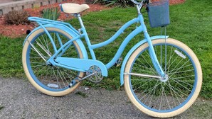 A blue bicycle with a basket and a seat, parked on a paved surface.