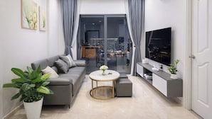 A modern living room with a sofa, a coffee table, a TV, and a balcony with a city view. - Monarchy Luxury Serviced Apartments (Da Nang)