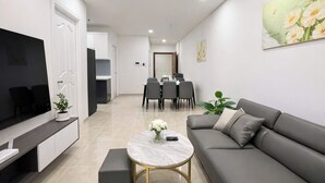 A modern living room with a sofa, a coffee table, a TV, and a dining area with chairs and a table. - Monarchy Luxury Serviced Apartments (Da Nang)