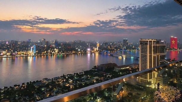 A cityscape at dusk with a river, illuminated buildings, and a prominent red building with a star. - Monarchy Luxury Serviced Apartments (Da Nang)