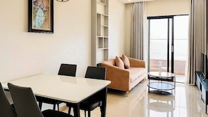 A modern living room with a dining area, a sofa, a coffee table, and a large window with curtains. - Monarchy Luxury Serviced Apartments (Da Nang)