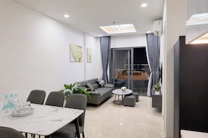 A modern living room with a sofa, dining table, and chairs, a balcony with curtains, and a city view.