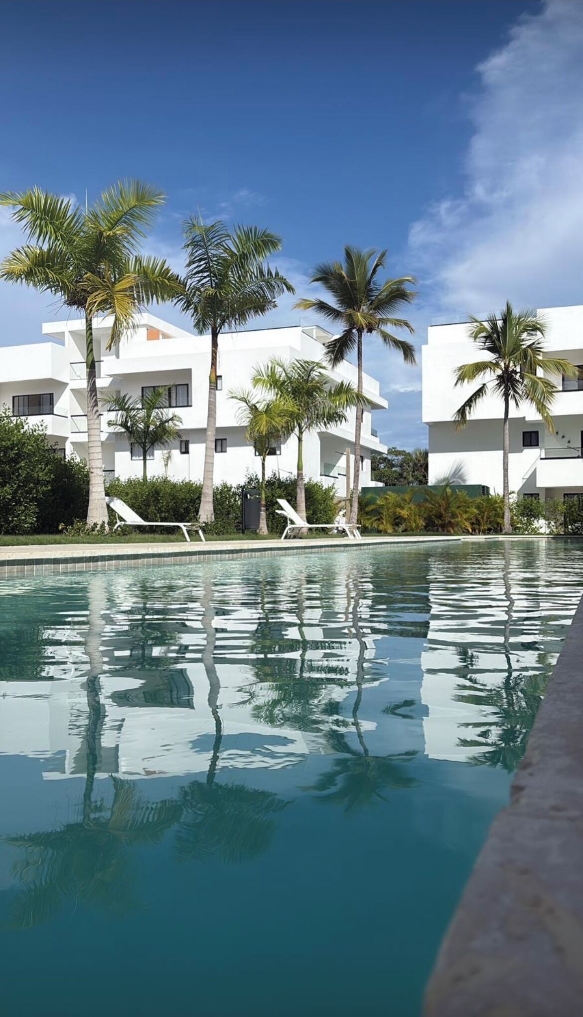 A modern hotel with white buildings, a swimming pool, and palm trees.