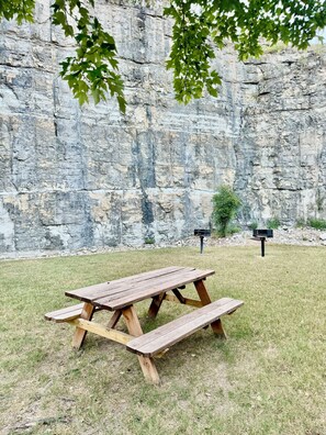 A picnic table in a grassy area with a rocky cliff in the background.
