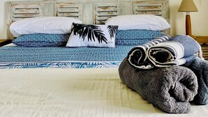 Une chambre d’hôtel avec un lit, un tableau représentant un arbre aux couleurs vives, des coussins à motifs et une serviette pliée.