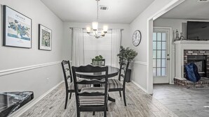A dining area with a round table, four chairs, a chandelier, framed artwork on the walls, and a fireplace in the background. - The VB Haven (Van Buren)