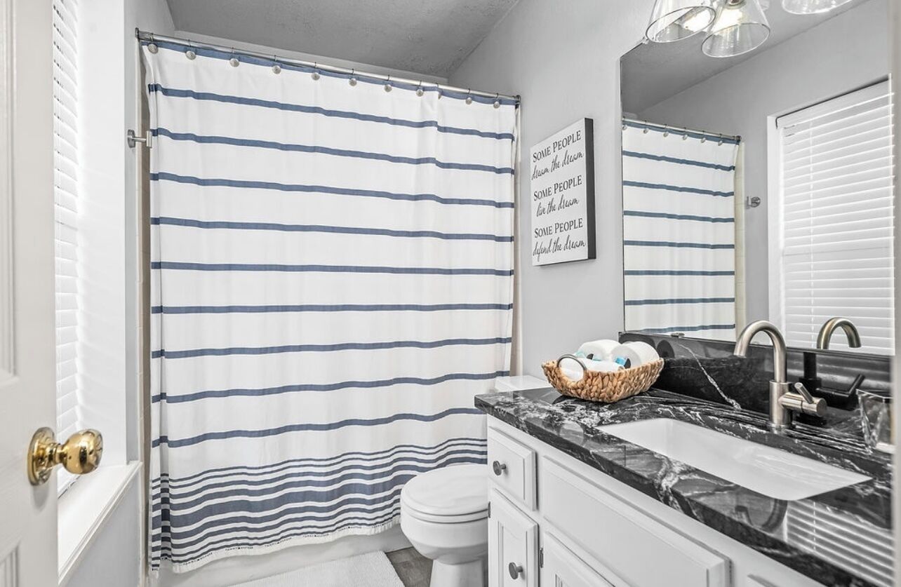 A bathroom with a striped shower curtain, a white toilet, a sink with a marble countertop, and a wall-mounted mirror.