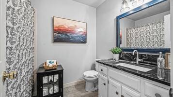 A bathroom with a black and white patterned shower curtain, a white toilet, a black cabinet with glass doors, a marble sink with a large mirror, and a framed painting on the wall.
