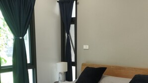 A neatly made bed with a wooden frame, a bedside table with a lamp, and a window with curtains.