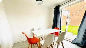A dining area with a white table and chairs, a black curtain, and a view of a brick building through a glass door.
