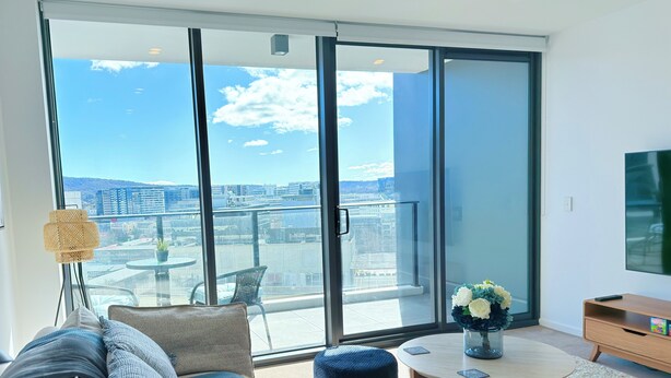 A modern living room with a large sliding glass door leading to a balcony, a sofa, a coffee table, and a TV.