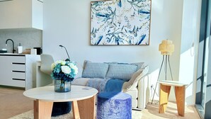 A modern living room with a sofa, a coffee table, and a side table. There is a painting on the wall and a lamp on the side table.