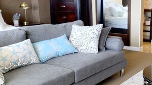 A modern hotel room with a grey sofa, decorative pillows, a dark wooden dresser, and a large mirror. - Ocean View Waikiki Luxury Ilikai Hotel~ (Honolulu)