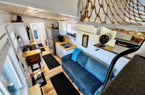 A compact kitchen with a sink, stove, and refrigerator. There is a blue sofa and a wooden dining table.
