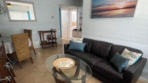 Ein Wohnzimmer mit einem Glastisch, einem dunklen Sofa und einem Gemälde an der Wand.