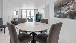 A modern dining area with a marble table and wicker chairs, large windows, and a cityscape painting on the wall.
