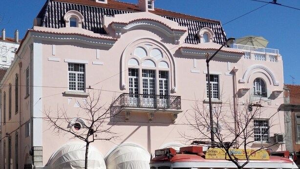 Un edificio rosa con un tranvía rojo y blanco en primer plano.