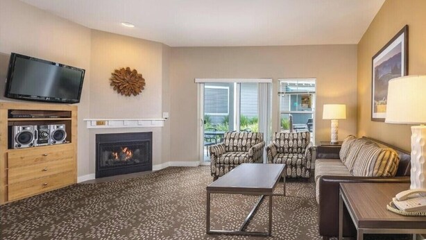 Un salon doté d’une cheminée, d’un téléviseur à écran plat, de fauteuils à motifs, d’un canapé et d’un balcon avec vue.