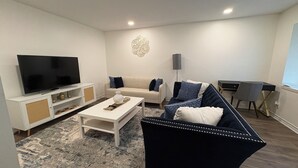 A modern living room with a flat-screen TV, a sofa, a coffee table, and a desk with a chair. - Updated Westbury Getaway Gem - 3 bedroom oasis (Houston)