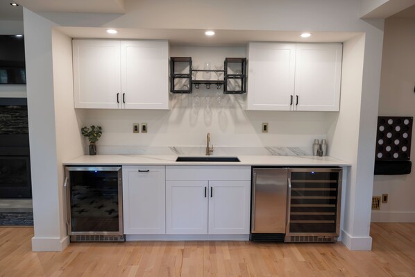 A modern kitchen with white cabinets, a stainless steel sink, and a built-in wine cooler.