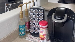 Una encimera de cocina con una cafetera, un dispensador de cápsulas de café y una botella de sirope.